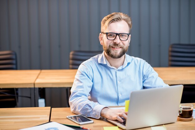 Man in blauw shirt aan het werk met laptop in het moderne kantoorinterieur