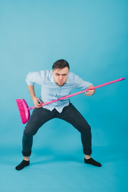 man in blauw shirt staat op blauwe achtergrond met roze bezem