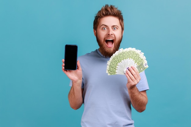 Man in blauw T-shirt met eurobankbiljetten en mobiele telefoon met lege display mock-up voor adverteren