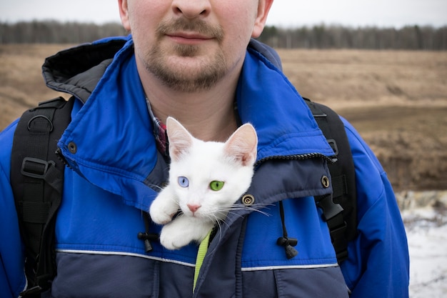 Man in blauwe jas met wit katje met blauwe en groene ogen in zijn boezem, close-up.