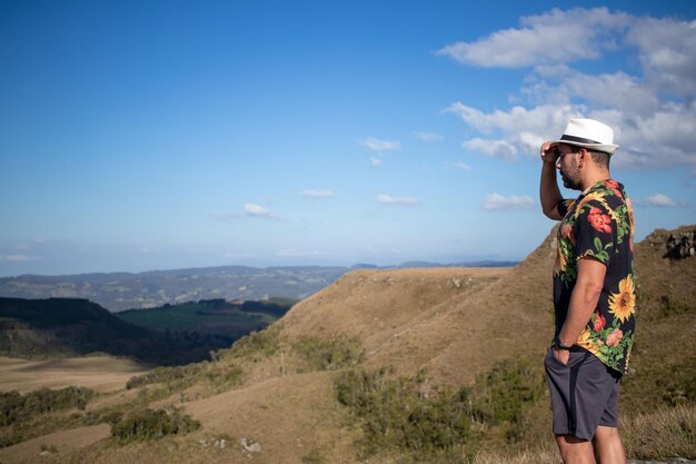 man in bloemrijke blouse die het landschap bewondert met een witte hoed op zijn hoofd