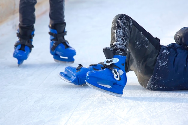 Фото Человек в синих коньках упал на лед. люди катаются на коньках на катке. хобби и спорт. каникулы и зимние развлечения.