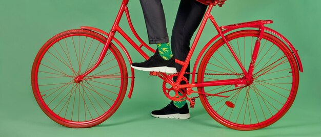 Foto man in broek heldere sokken en zwarte suède sneakers rode vintage fiets rijden op groene studio achtergrond bijgesneden schot concept van comfortabele casual schoenen