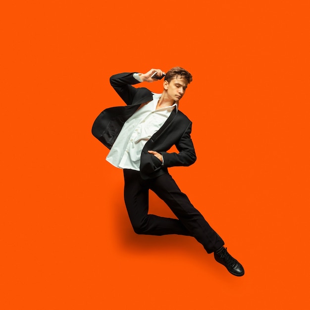 Man in casual kleding in kantoorstijl springen en dansen geïsoleerd op fel oranje achtergrond. Bedrijf, start-up, open ruimte, inspiratieconcept. Flexibele balletdans. Opschieten, koffie drinken.
