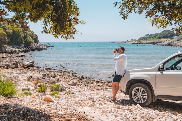 Man in de buurt van witte suv auto op zomer zee strand vrijheid reizen concept