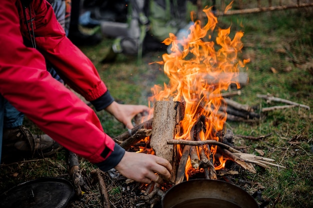 Man in de rode jas die een brandhout plaatst bij het kampvuur in het bos in Georgië in de winter