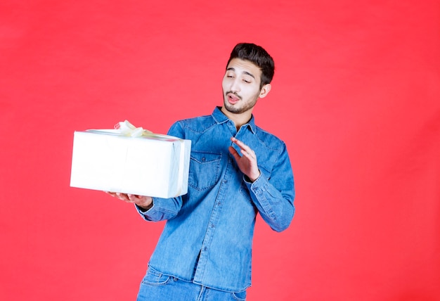 Man in denim shirt met zilveren geschenkdoos en weigering geven.