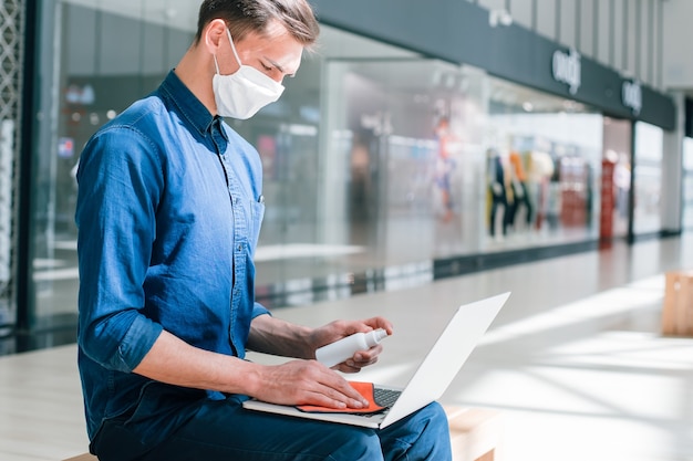 Man in een beschermend masker desinfecteert zijn laptop. pandemie in de stad