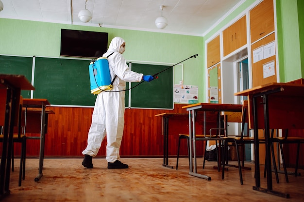 Man in een beschermend pak die een klaslokaal desinfecteert