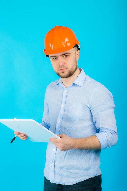 man in een blauw shirt in een beschermende oranje helm en een wit notitieboekje staat op een blauwe achtergrond