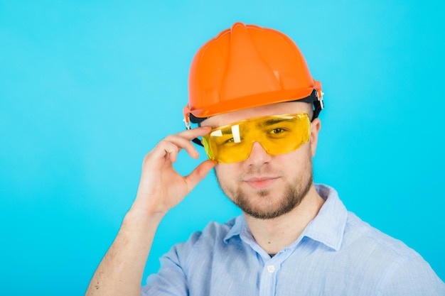 man in een blauw shirt in een beschermende oranje helm en een wit notitieboekje staat op een blauwe achtergrond