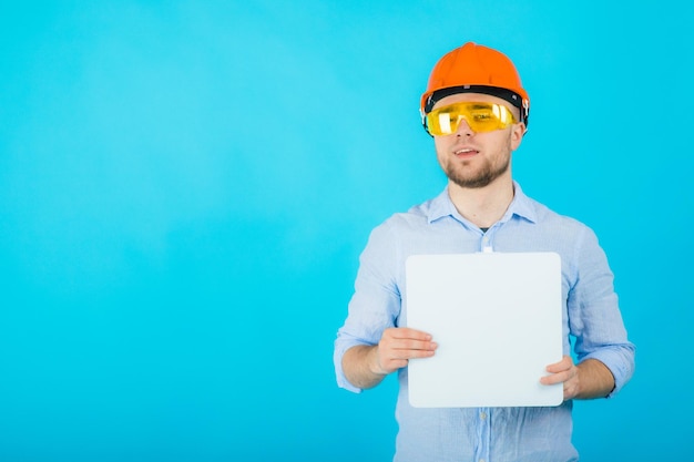 man in een blauw shirt in een beschermende oranje helm en een wit notitieboekje staat op een blauwe achtergrond