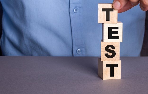 Man in een blauw shirt stelt het woord TEST verticaal samen uit houten kubussen