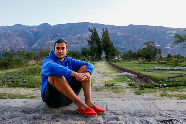 Man in een blauw shirt zittend op stenen in een groen veld en bomen bij zonsondergang.