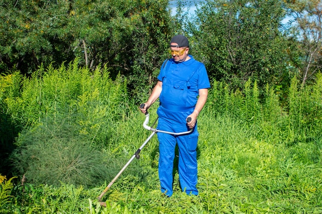 Man in een blauwe jumpsuit het gras maaien met een trimmer.