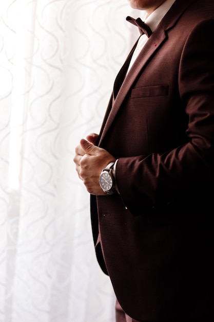 Man in een elegante bruine smoking met een zijden vlinderdas en een horloge