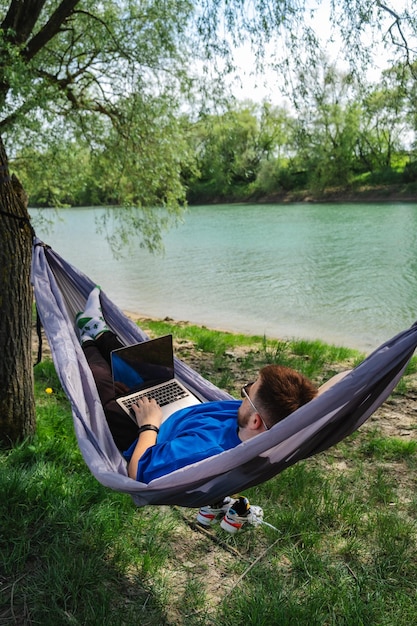 Man in een hangmat met laptop bij de rivier Ontspannende werkomgeving