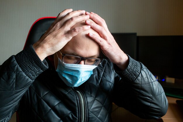 Man in een medisch masker houdt zijn handen in de buurt van zijn voorhoofd.