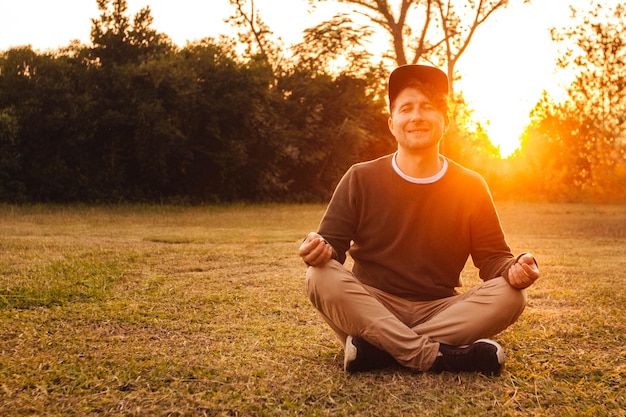 man in een meditatieve positie zit op een grasveld op een achtergrond van bos en zonsondergang