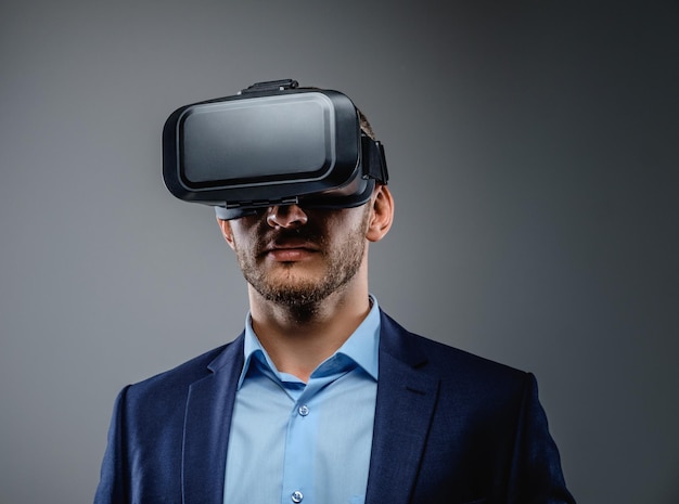 Man in een pak met virtual reality-bril op zijn hoofd. Geïsoleerd op grijze achtergrond.