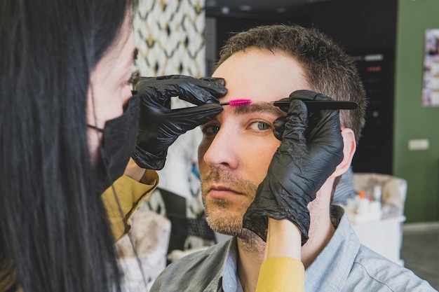 Man in een schoonheidssalon tijdens de wenkbrauw aanpassingsprocedure Een vrouw verwijdert overtollig haar op het gezicht van een man