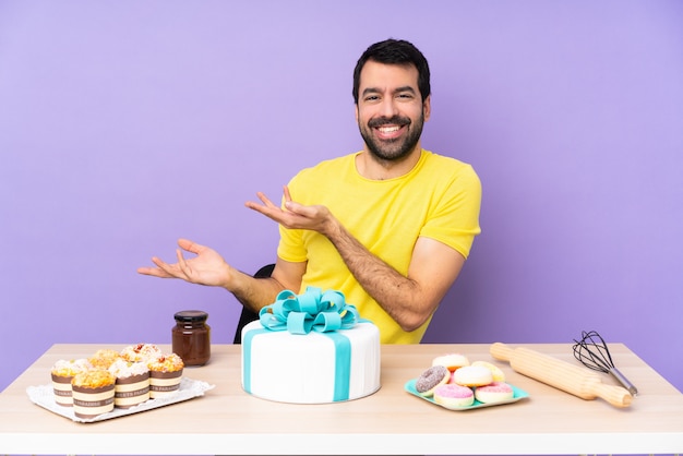 Man in een tafel met een grote cake die handen naar de zijkant uitstrekt om uit te nodigen om te komen