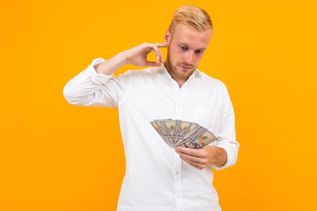 Man in een wit overhemd denkt na over wat hij verdiende geld moet uitgeven op een gele achtergrond met kopie ruimte.