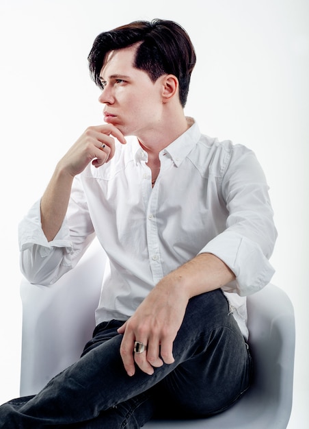 man in een wit overhemd zit op een stoel op een witte achtergrond, de man poseren in een stoel in de studio - geïsoleerd