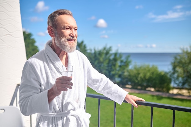 Man in een witte badjas die op het balkon staat