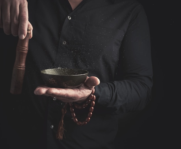 Man in een zwart shirt draait een houten stok rond een koperen Tibetaanse kom met water. ritueel van meditatie