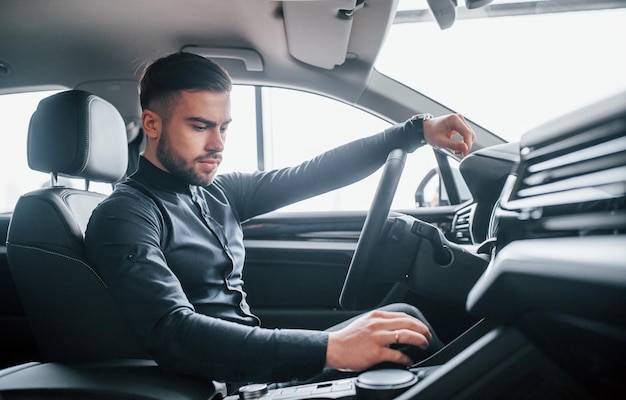 Man in elegante kleding zittend in gloednieuwe dure auto.