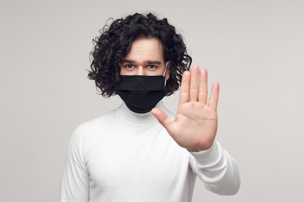 사진 얼굴에 마스크를 쓴 남자가 사회적 거리를 유지하기 위해 손짓을 합니다.