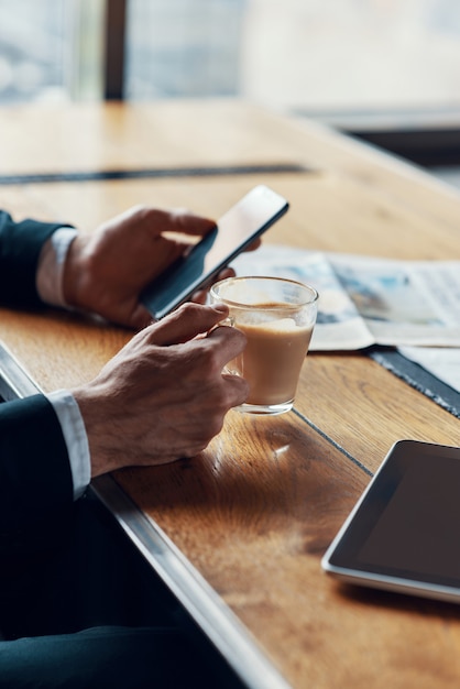 man in formalwear met behulp van slimme telefoon en kopje koffie te houden