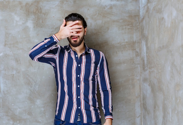 Foto man in gestreept shirt kijkt over vingers.