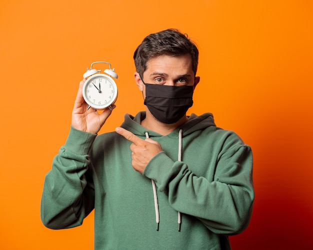 Man in gezichtsmasker en groene hoodie met wekker op oranje