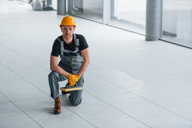 Man in grijs uniform poseren voor een camera binnenshuis in een modern groot kantoor overdag