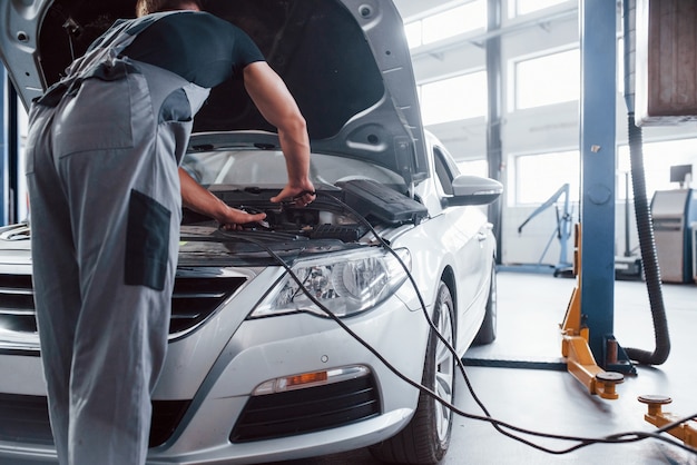 Man in grijs uniform repareert witte auto binnenshuis