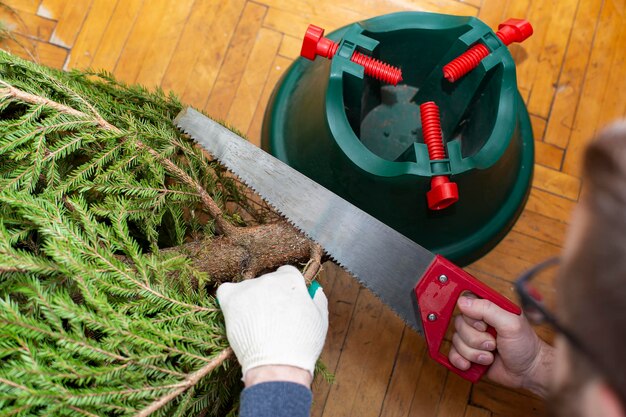 Man in handschoenen die een zaag gebruikt, zaagt takken op de stam van een kerstboom