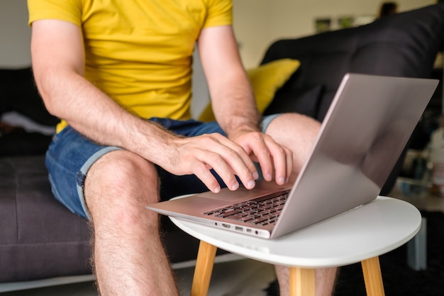 Man in het gele t-shirt typen op de laptop zittend in de moderne woonkamer freelancer aan het werk