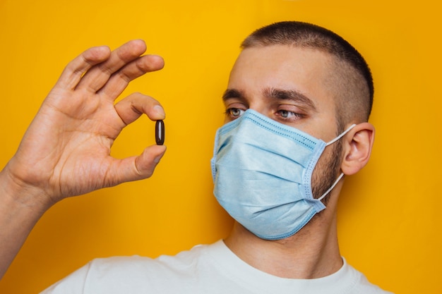 Man in het masker houdt een pil van het coronavirus in zijn handen. vitaminen om het immuunsysteem te versterken. ga thuis zitten. verkoudheid, griep, virus, quarantaine, epidemisch concept. moeilijke keuze.