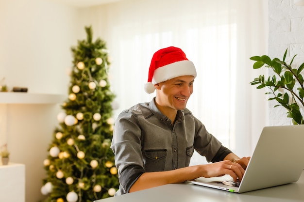 man in kerstman hoed met laptop met vrolijk kerstfeest typen