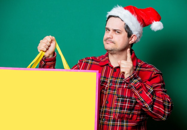 Man in kerstmuts en tartan shirt met boodschappentas op groen