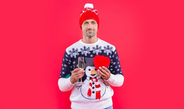 Man in kerstmuts met champagne en hart kerst man geïsoleerd op rode achtergrond