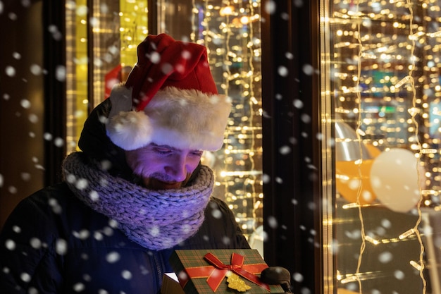 Man in kerstmuts met geschenkdoos in de buurt van verlicht caféraam