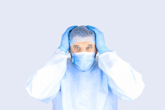 Фото Мужчина в медицинском халате, маске и перчатках держит голову, показывая жест ужаса
