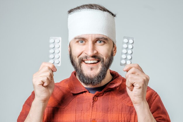 Foto man in medisch verband met pillen in een hand geïsoleerd op een grijze achtergrond