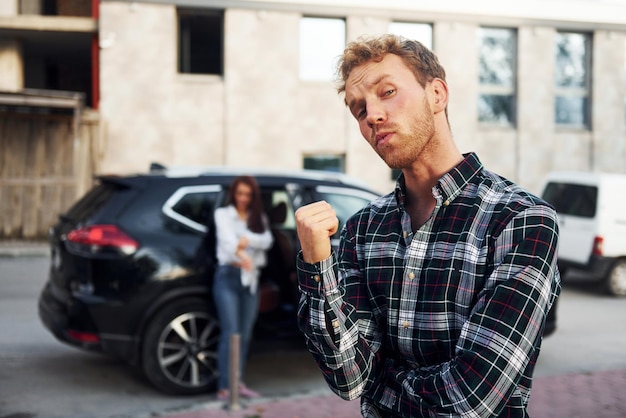 Man in modieuze kleding die voor een meisje staat dat in de buurt van de zwarte auto staat