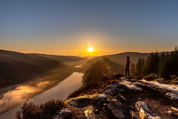 Man in oranje jasje die op de Spink Viewing Spot staat en de zonsopgang in Wicklow Ierland bewondert