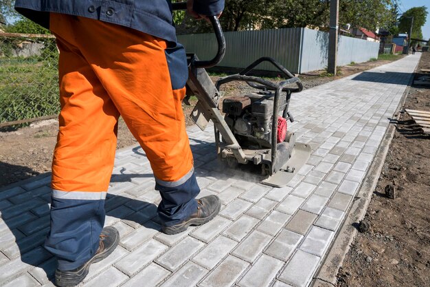 Foto man in oranje uniform met vibrerende straatsteenmachine voor afwerking op een trottoir