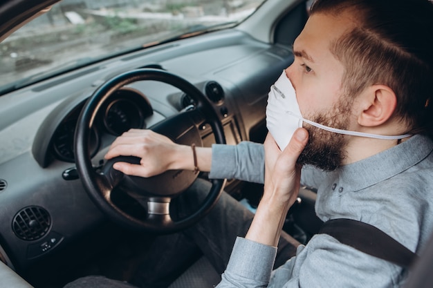 man in overhemd en medische masker zit achter het stuur van de auto.